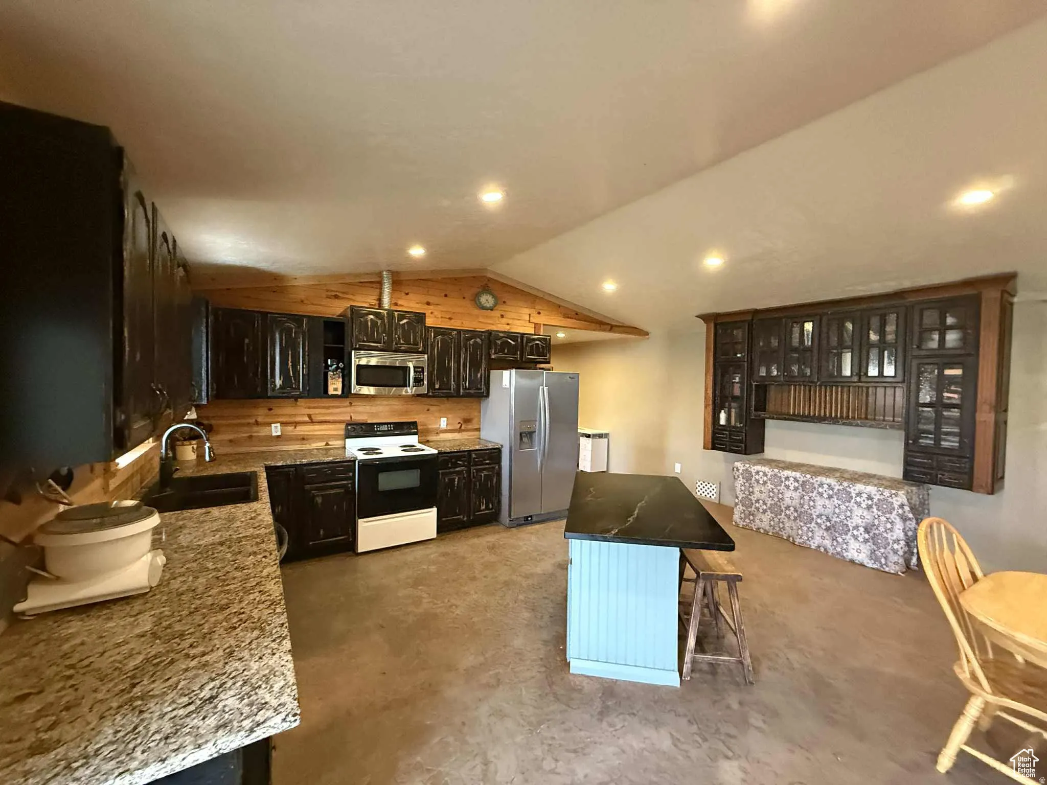 Kitchen featuring appliances with stainless steel finishes, a center island, vaulted ceiling, dark stone countertops, and finished concrete flooring