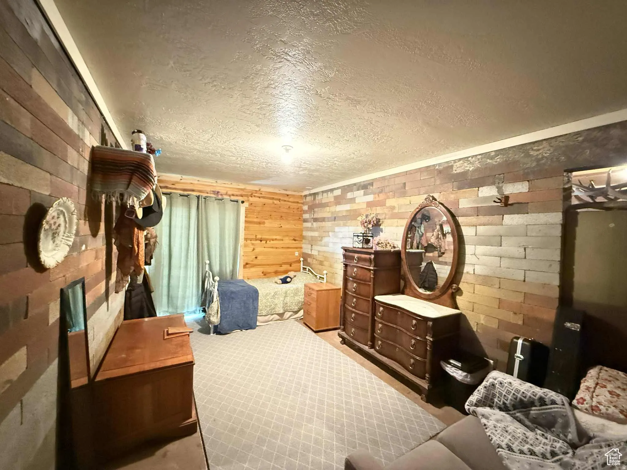 Carpeted bedroom featuring a textured ceiling, wooden walls, and brick wall