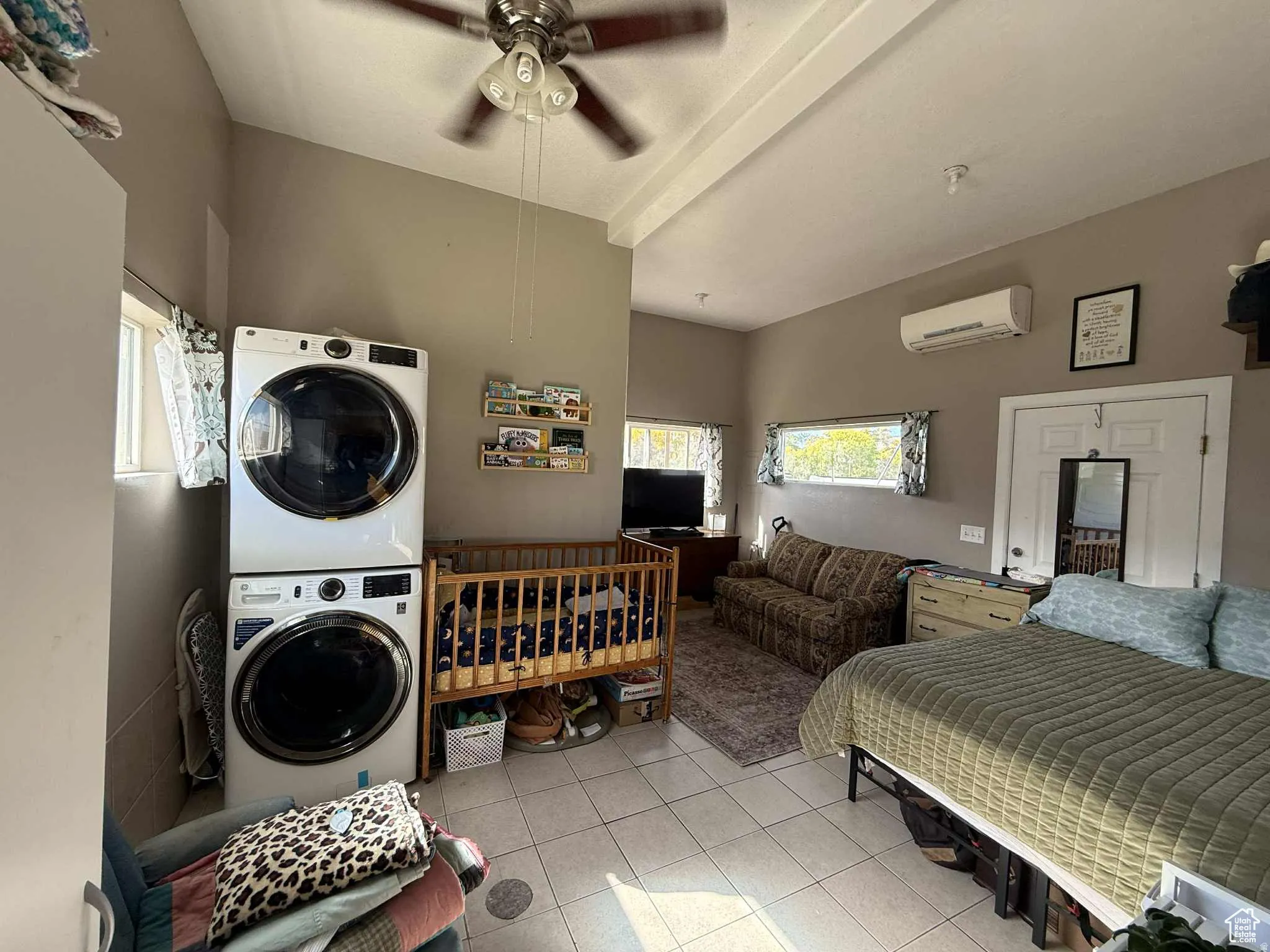 Laundry room featuring stacked washer / dryer, light tile patterned flooring, ceiling fan, and a wall unit AC