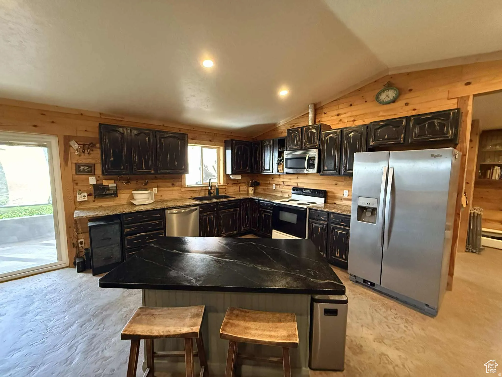 Kitchen featuring wood walls, appliances with stainless steel finishes, vaulted ceiling, a kitchen island, and a breakfast bar