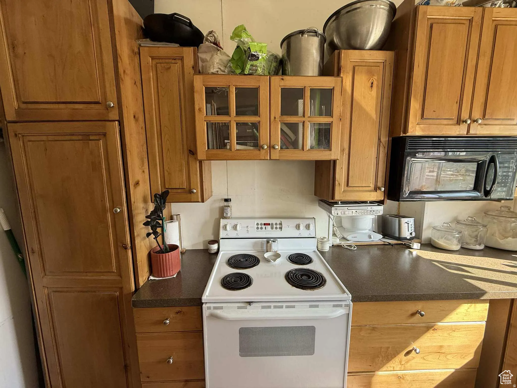Kitchen featuring dark countertops, electric range, glass insert cabinets, black microwave, and brown cabinetry