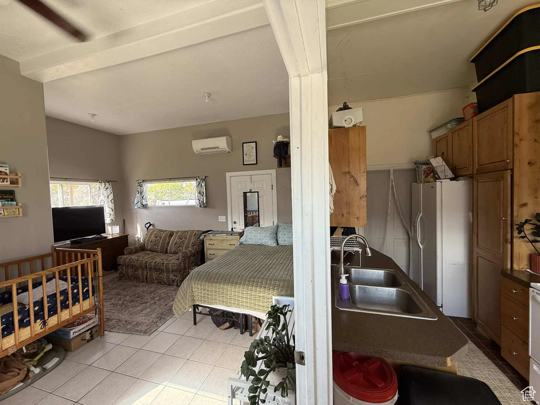 Bedroom featuring white refrigerator with ice dispenser, light tile patterned flooring, and a wall mounted AC