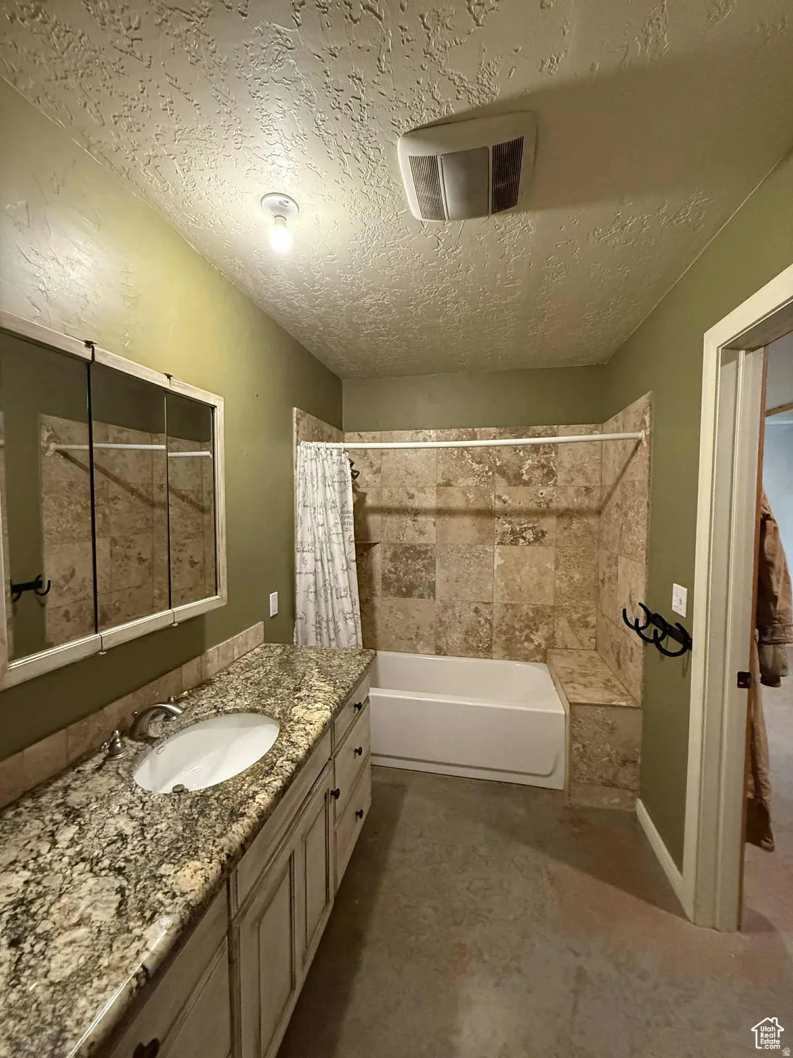 Bathroom featuring shower / tub combo with curtain, vanity, a textured ceiling, and concrete flooring