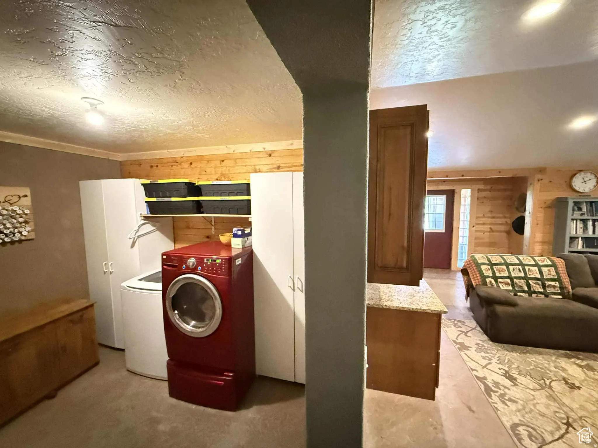 Washroom with a textured ceiling, wooden walls, and washing machine and dryer