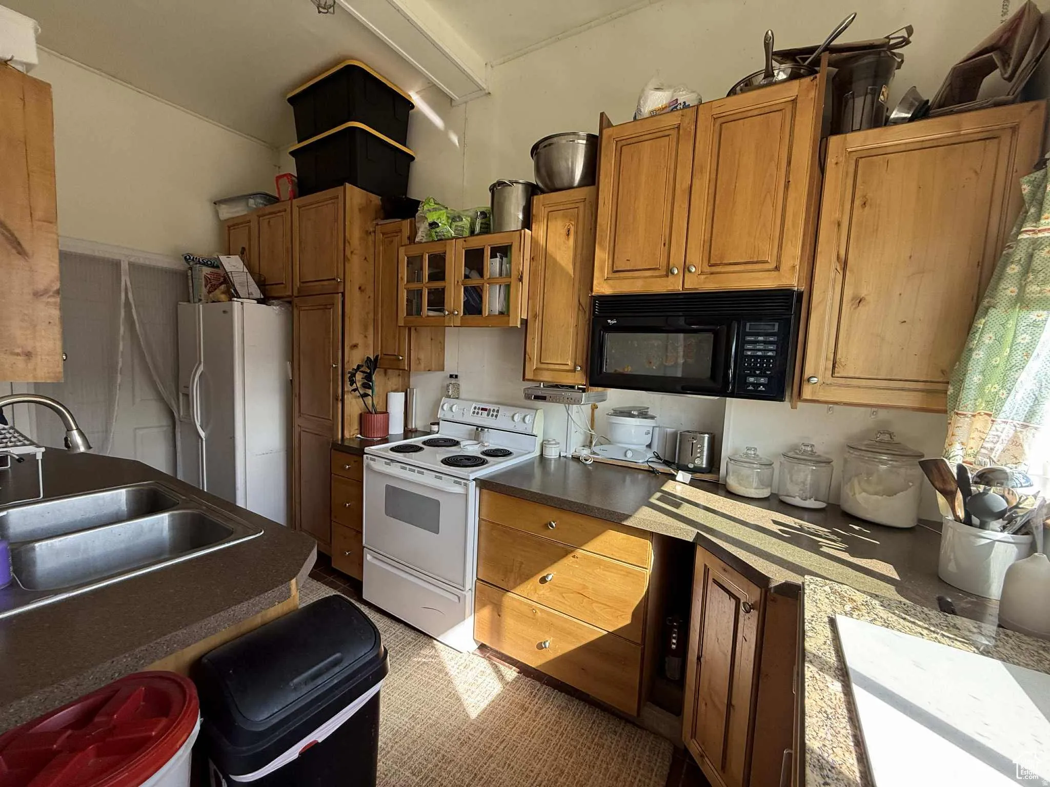 Kitchen with white appliances, brown cabinetry, dark countertops, and glass insert cabinets