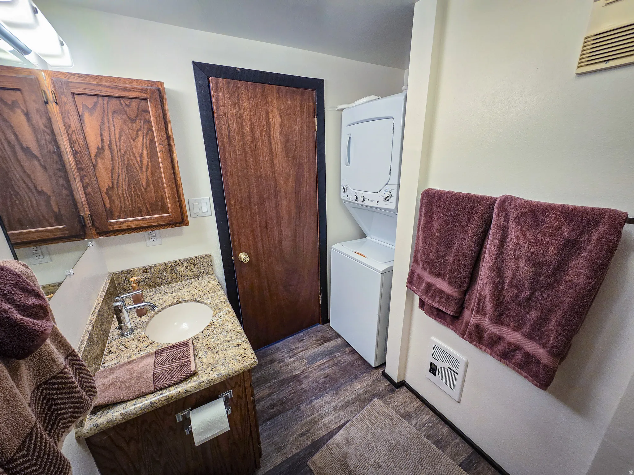 Half bathroom featuring vanity, stacked washing machine and dryer, dark wood finished floors, and heating unit