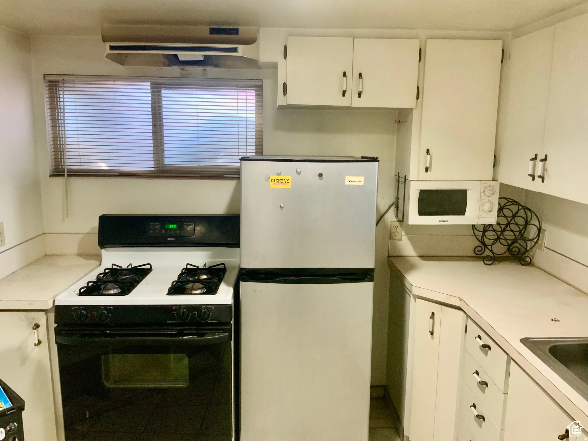 Kitchen with gas range oven, light countertops, white cabinets, and freestanding refrigerator