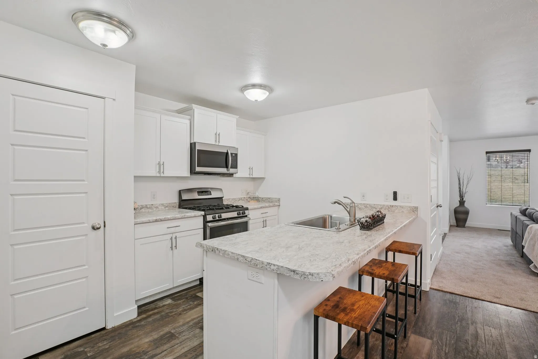 Kitchen with a kitchen bar, stainless steel appliances, light countertops, white cabinets, and dark wood finished floors