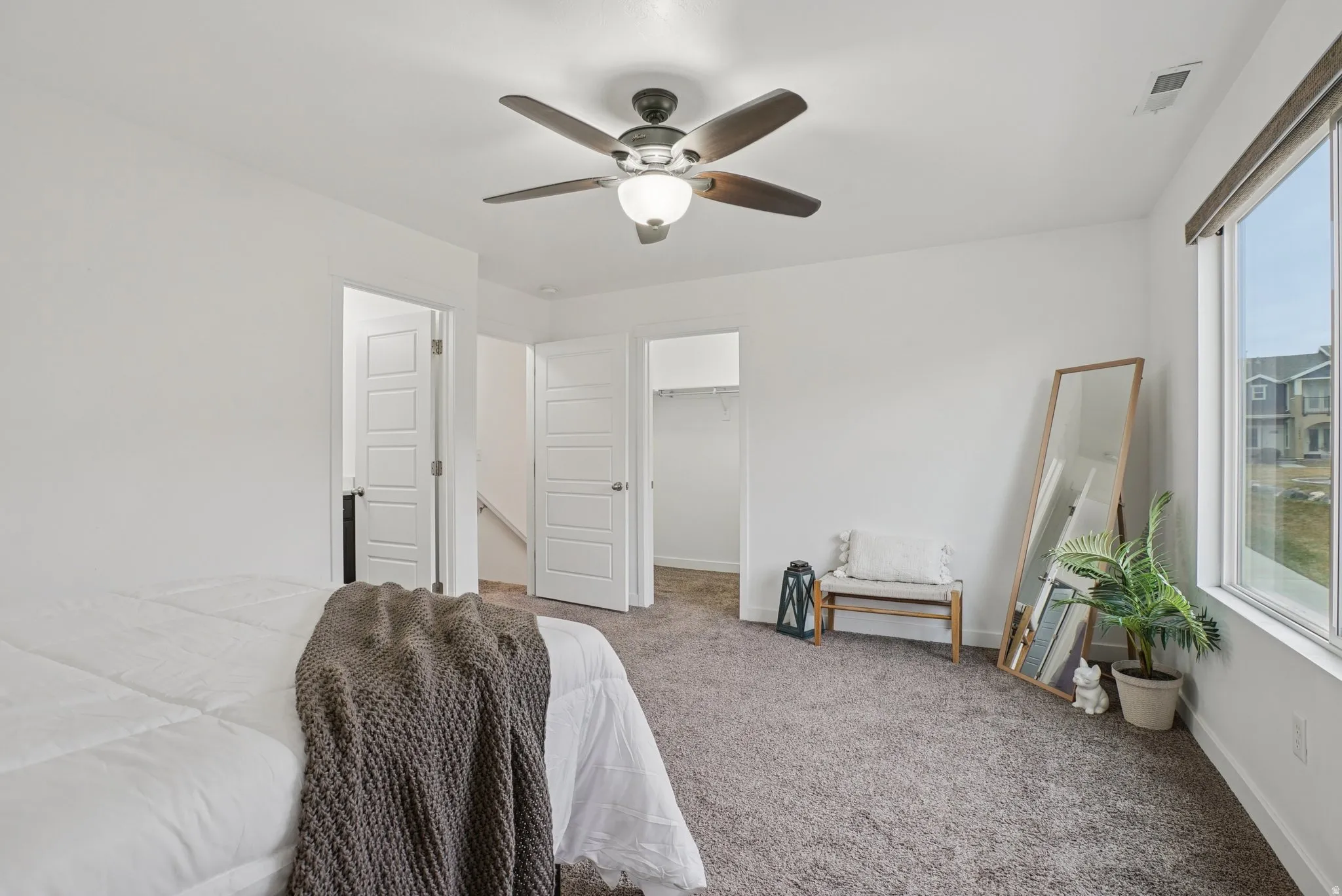 Bedroom featuring a walk in closet, carpet flooring, ceiling fan, and multiple windows
