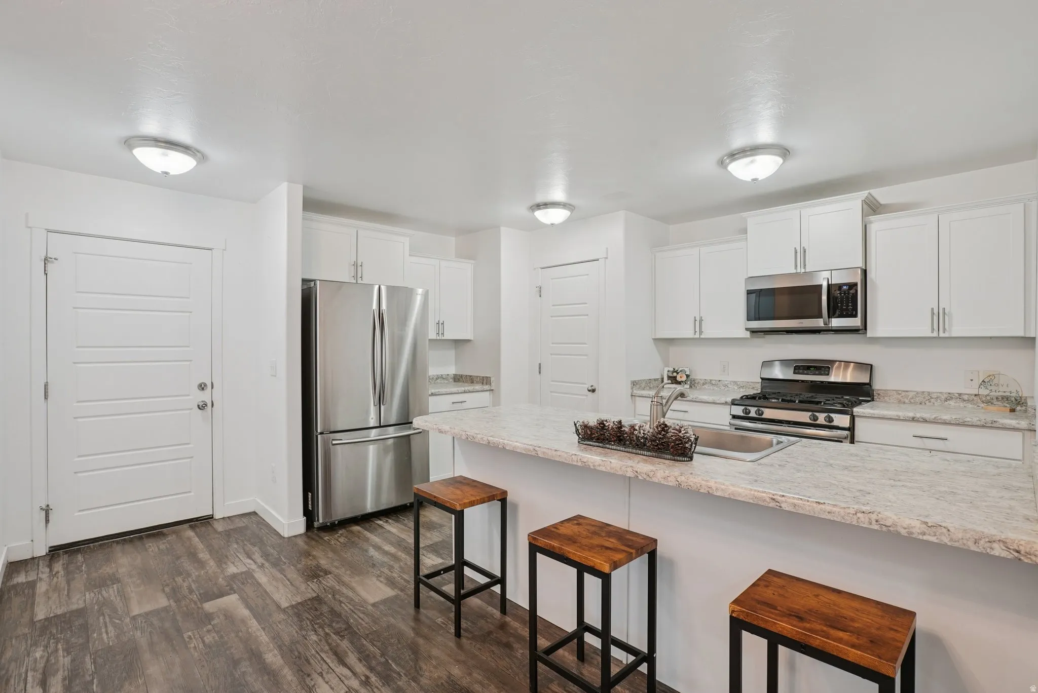 Kitchen with a breakfast bar, appliances with stainless steel finishes, white cabinets, and dark wood-style floors
