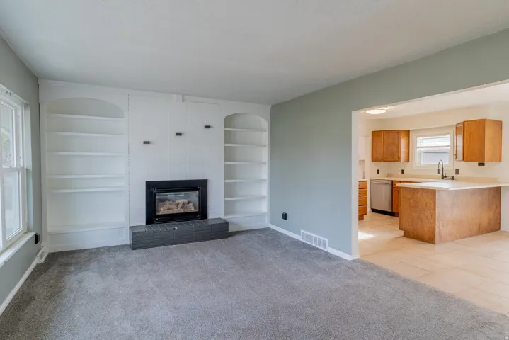 Unfurnished living room featuring built in features, a large fireplace, and light carpet