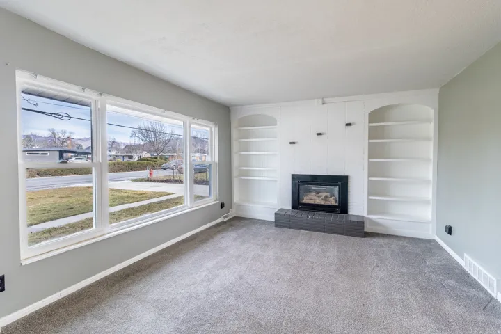 Unfurnished living room with built in shelves, a brick fireplace, light colored carpet, and a textured ceiling