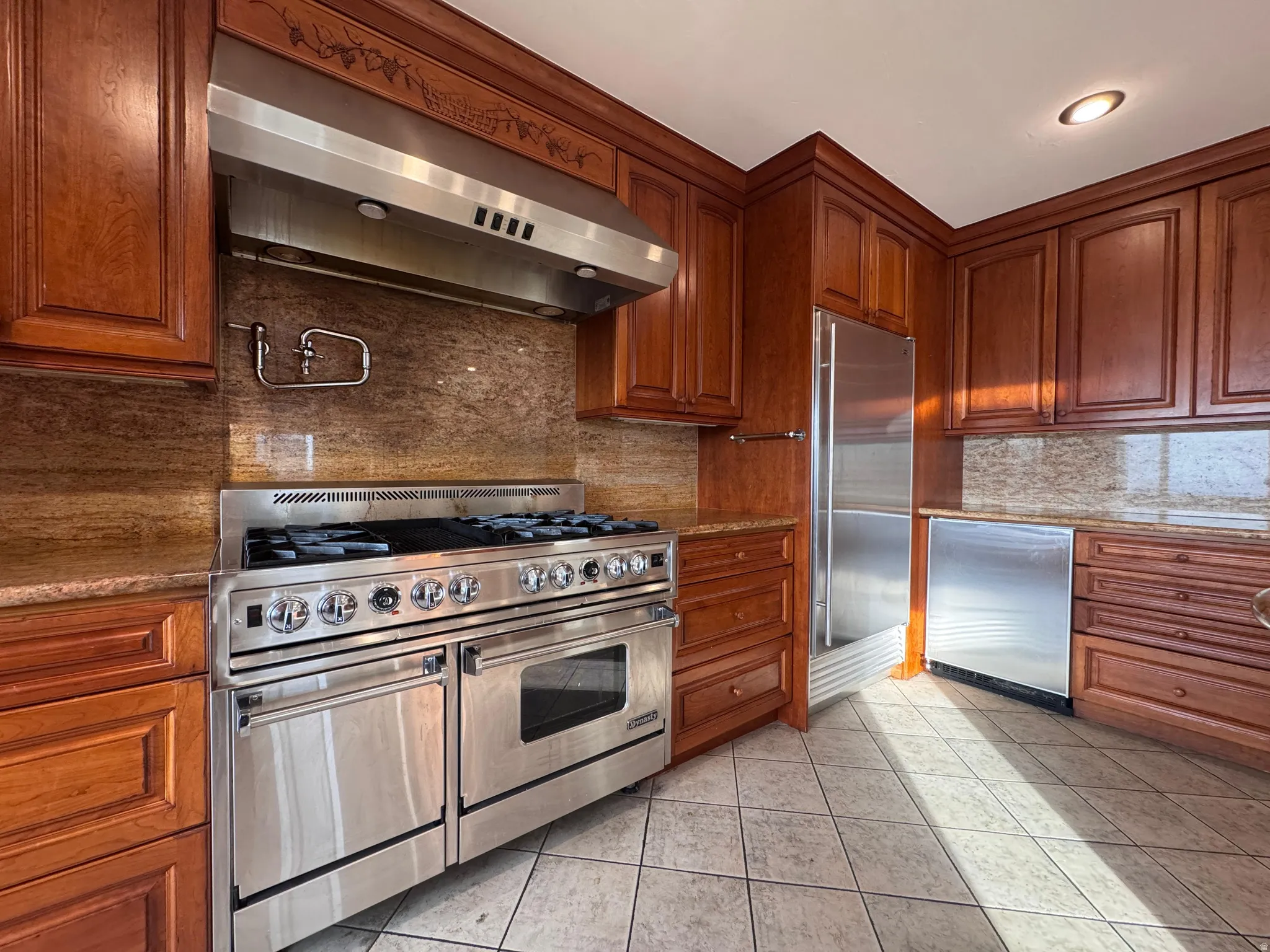 Kitchen with high quality appliances, exhaust hood, light stone counters, and decorative backsplash