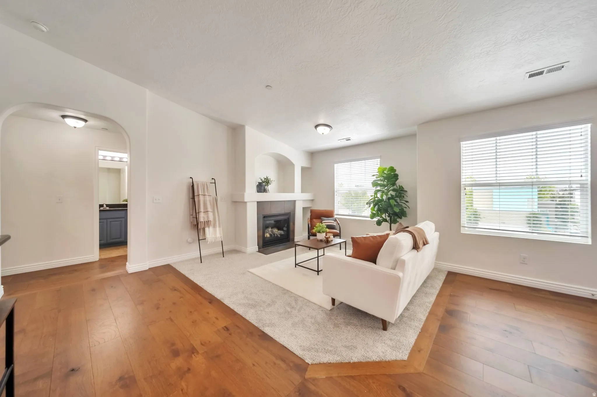 Living area featuring arched walkways, wood-type flooring, a fireplace, and a textured ceiling