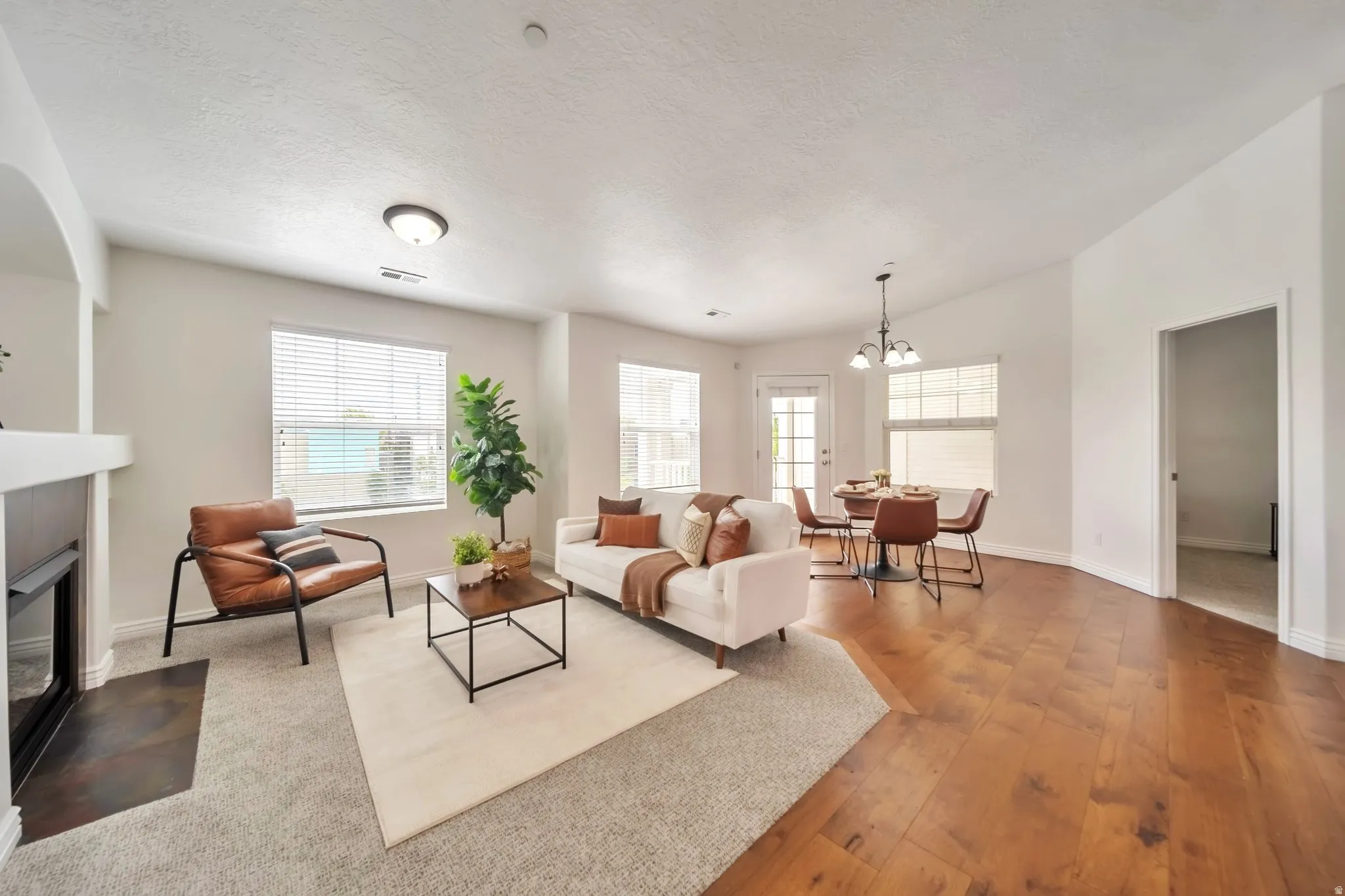 Living area with a textured ceiling, a chandelier, a fireplace with flush hearth, plenty of natural light, and light wood-style floors