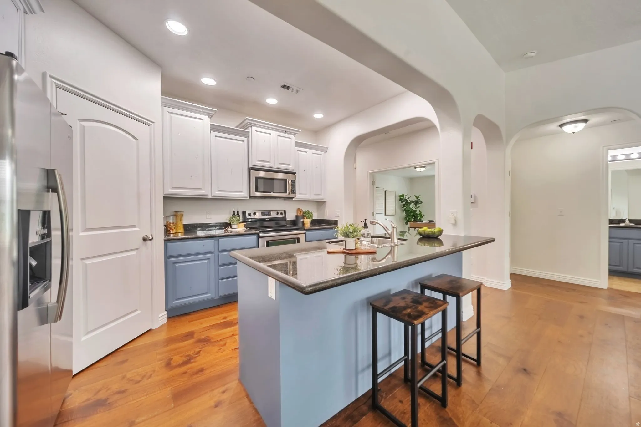 Kitchen with appliances with stainless steel finishes, a kitchen breakfast bar, white cabinetry, light wood finished floors, and arched walkways