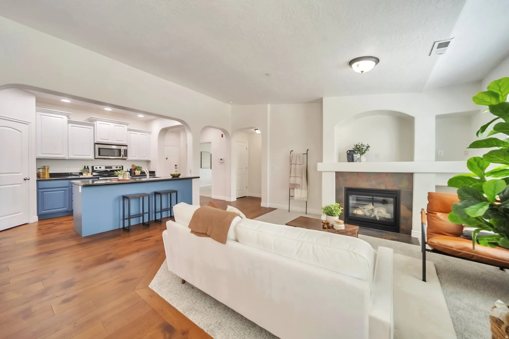 Living area featuring arched walkways, a tile fireplace, dark wood finished floors, recessed lighting, and a textured ceiling
