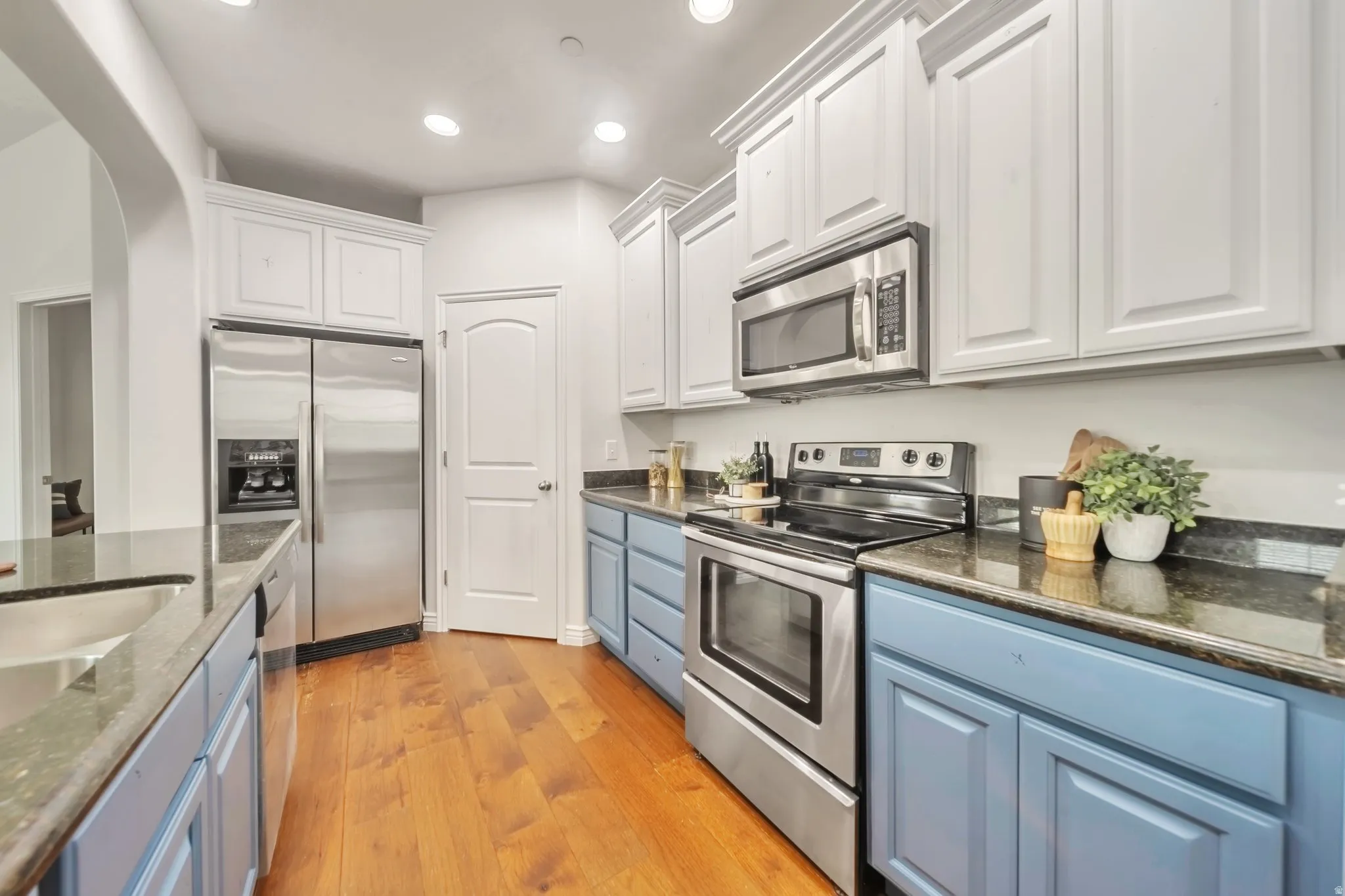 Kitchen featuring appliances with stainless steel finishes, white cabinets, dark stone counters, blue cabinetry, and recessed lighting