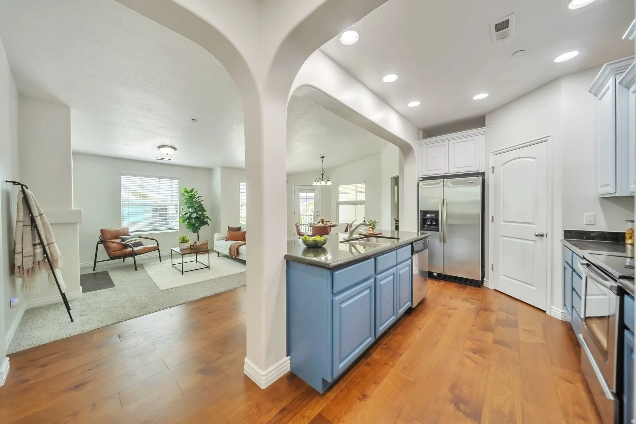 Kitchen featuring blue cabinetry, hanging light fixtures, stainless steel appliances, light wood-style flooring, and plenty of natural light