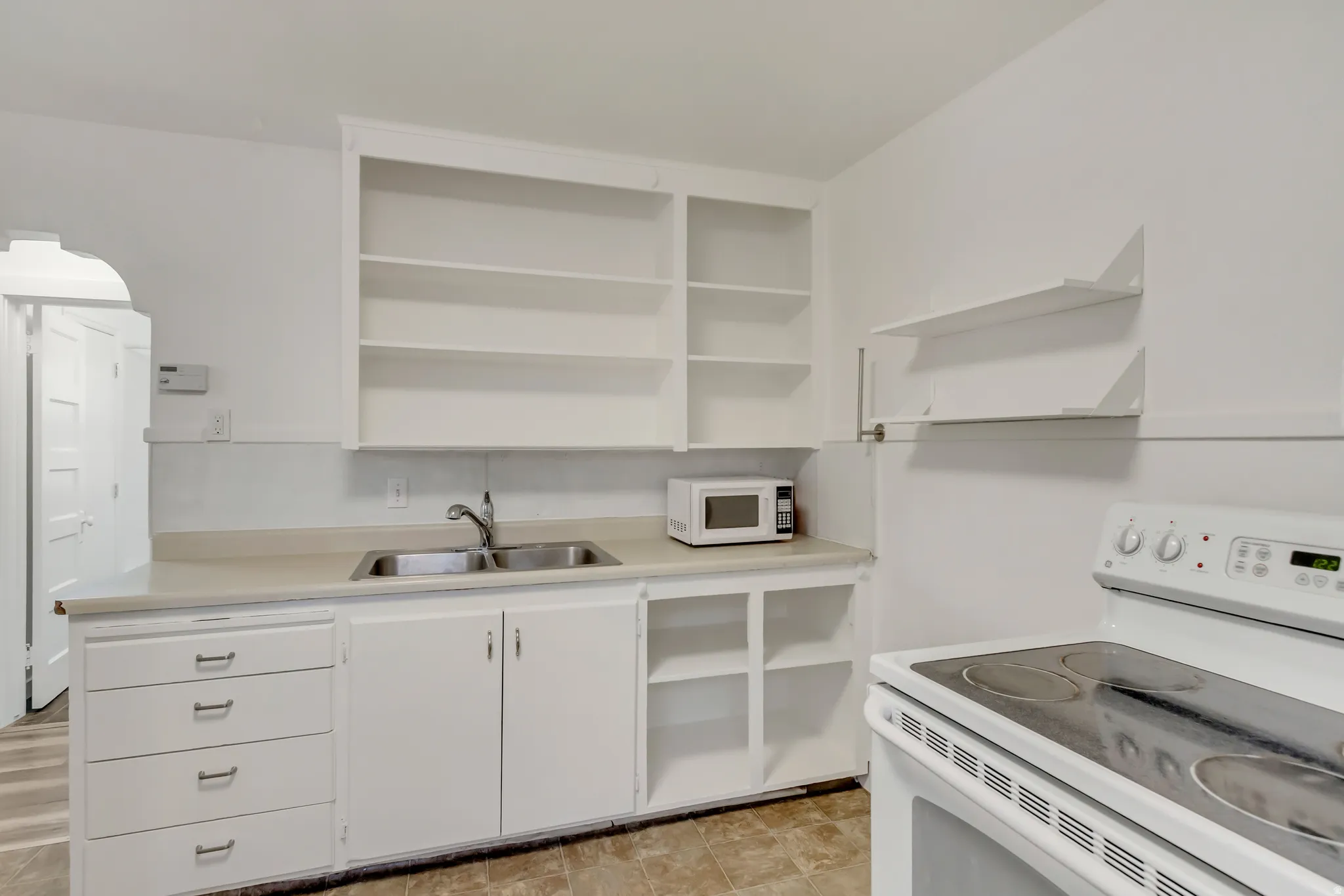 Kitchen with open shelves, white appliances, white cabinetry, and light countertops