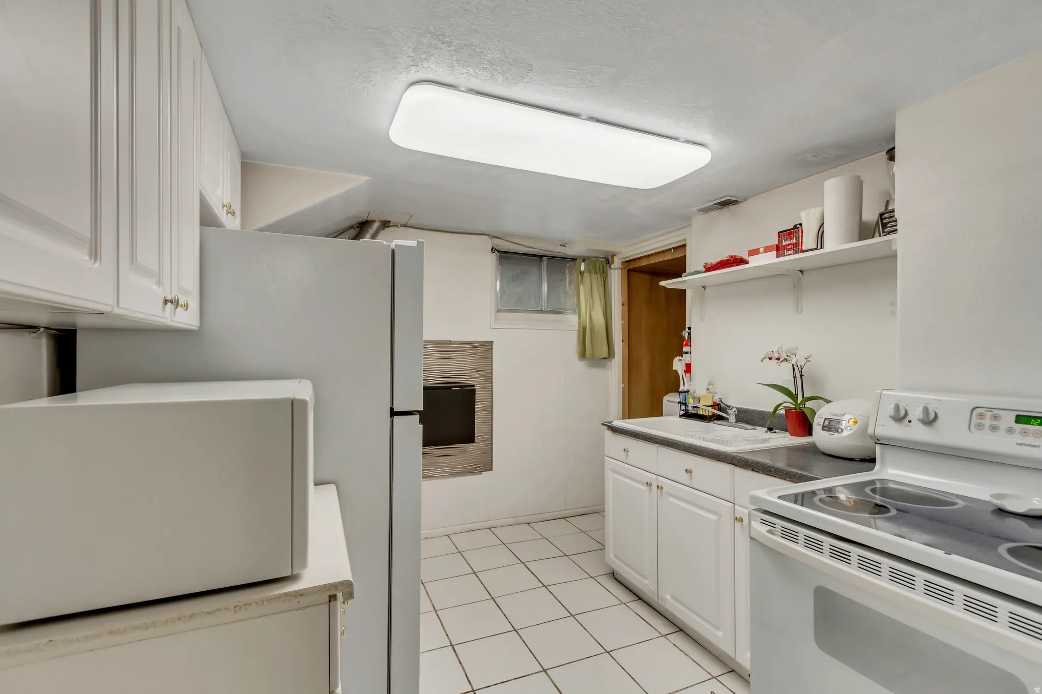 Kitchen with white appliances, white cabinetry, open shelves, light tile patterned floors, and a textured ceiling