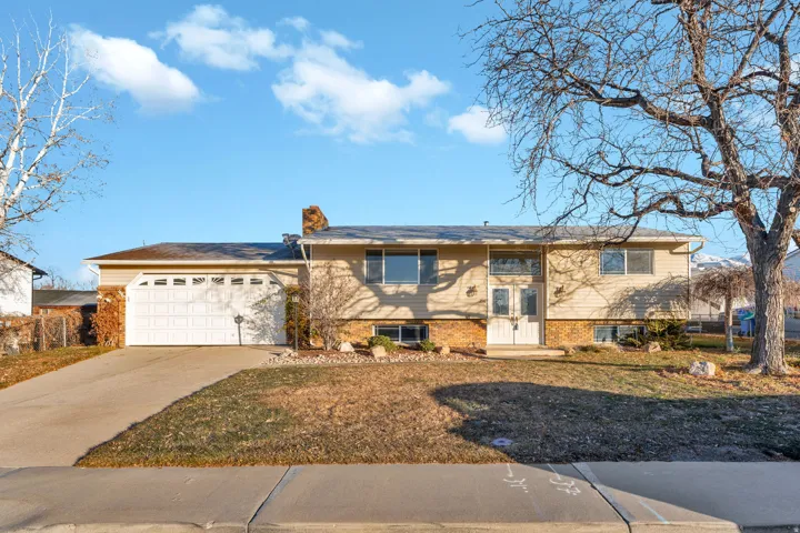 Bi-level home featuring concrete driveway, a chimney, brick siding, a front yard, and an attached garage