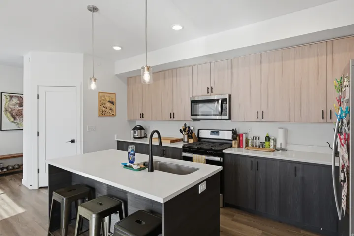 Kitchen featuring light brown cabinetry, a breakfast bar area, an island with sink, pendant lighting, and appliances with stainless steel finishes