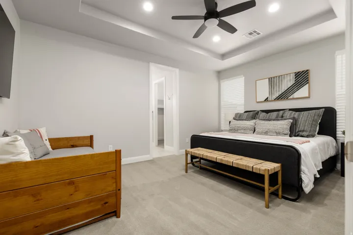 Primary bedroom featuring a tray ceiling, light colored carpet, recessed lighting, and a ceiling fan