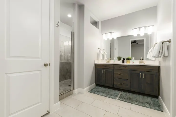 Primary bathroom featuring double vanity, light tile patterned floors, a shower stall, and a ceiling fan