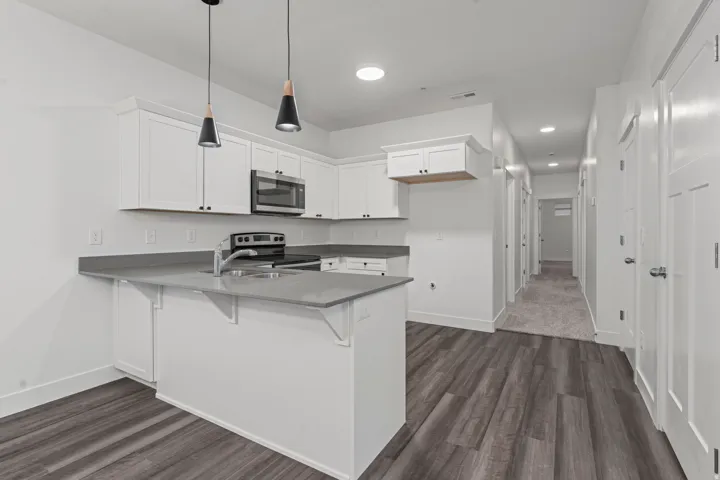 Kitchen featuring white cabinetry, a peninsula, appliances with stainless steel finishes, decorative light fixtures, and a kitchen breakfast bar