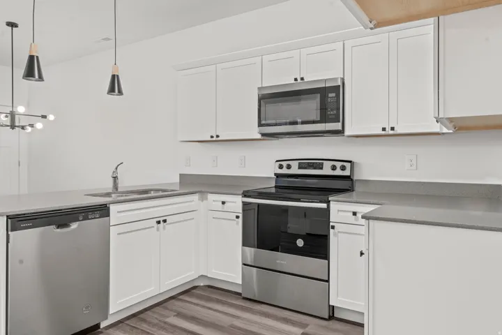 Kitchen with appliances with stainless steel finishes, white cabinetry, a peninsula, decorative light fixtures, and light wood-style flooring