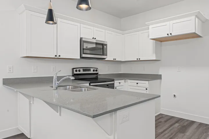 Kitchen with stainless steel appliances, pendant lighting, white cabinetry, a peninsula, and dark stone countertops