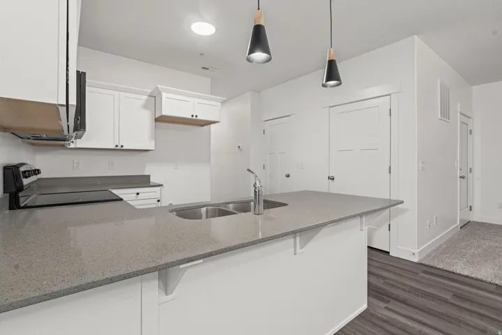 Kitchen featuring a peninsula, a kitchen breakfast bar, dark stone countertops, black electric range, and white cabinetry