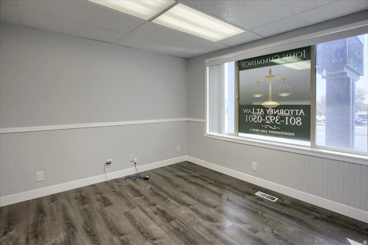 Unfurnished room featuring a drop ceiling, dark wood-style floors, wainscoting, and wooden walls