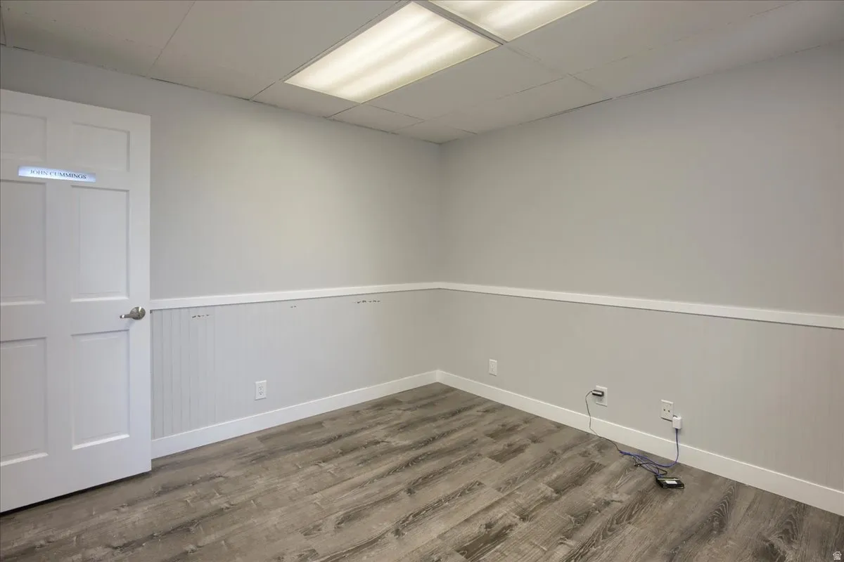 Empty room with a drop ceiling, wood finished floors, and a wainscoted wall