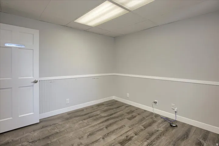 Empty room with a drop ceiling, wood finished floors, and a wainscoted wall