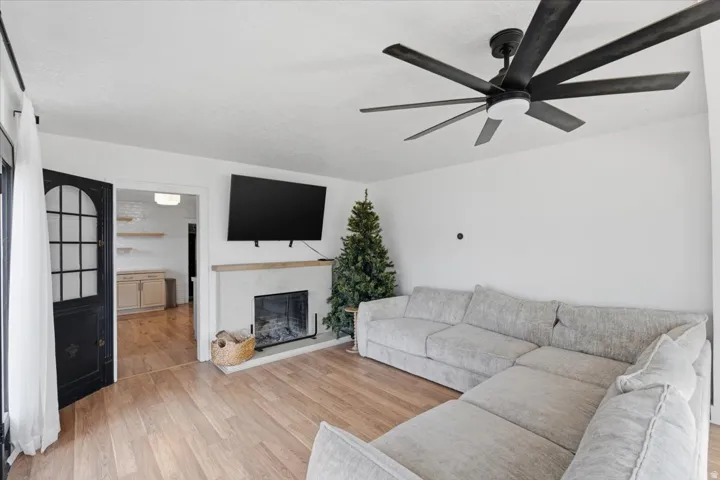 Living area with light wood-type flooring, a glass covered fireplace, and ceiling fan