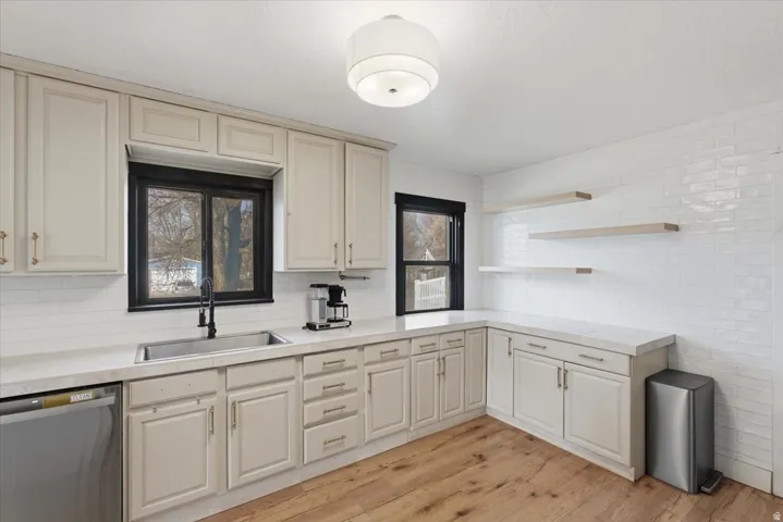 Kitchen featuring dishwasher, light countertops, open shelves, light wood finished floors, and tasteful backsplash