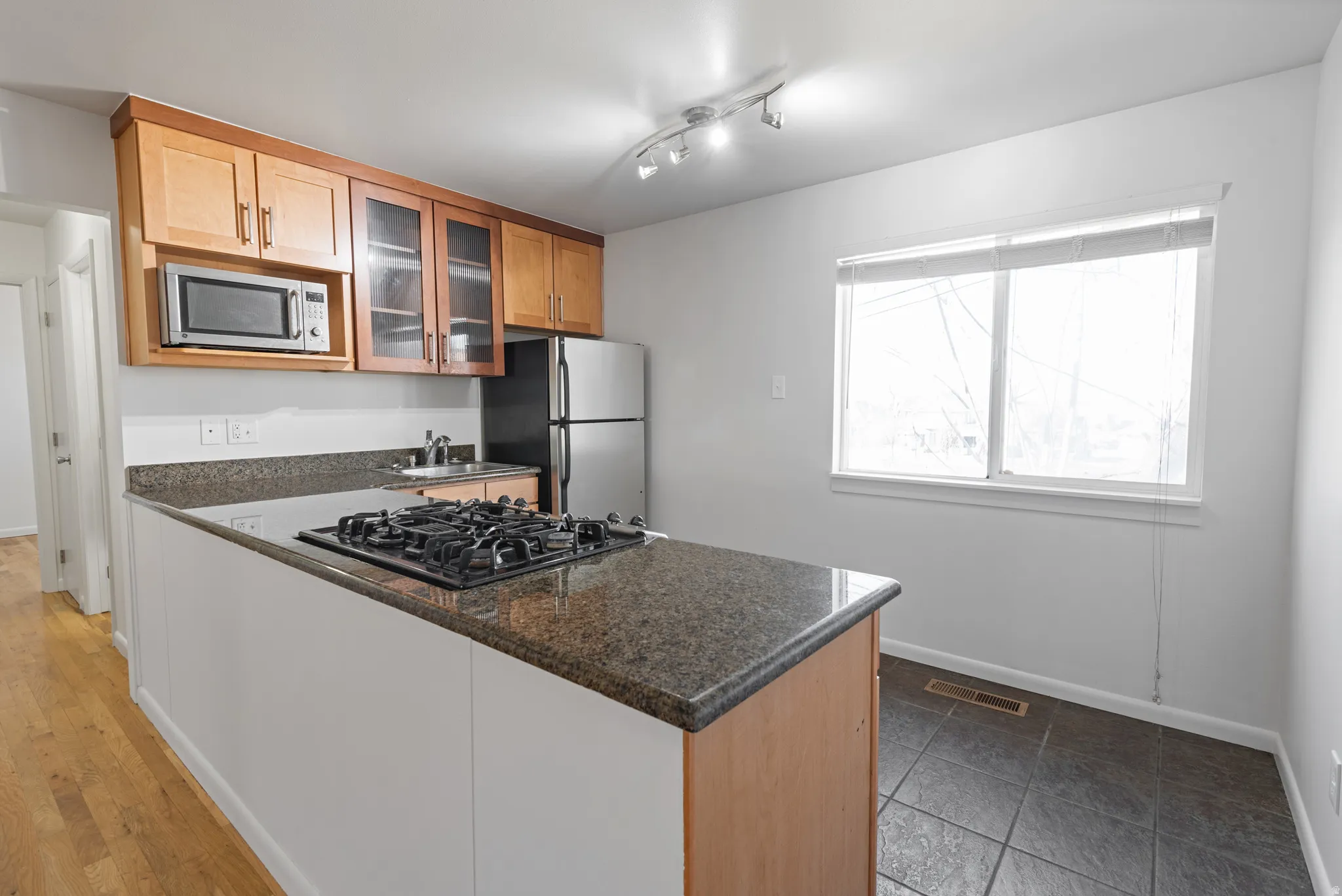Kitchen with glass insert cabinets, stainless steel appliances, dark stone countertops, and track lighting