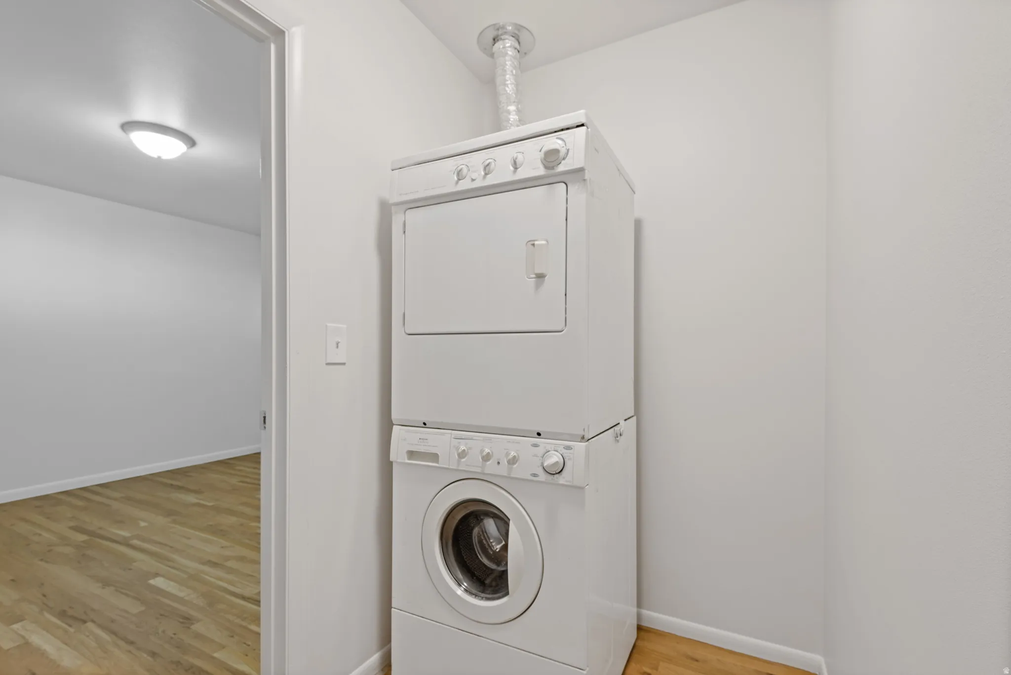 Washroom featuring light wood finished floors and stacked washing machine and dryer