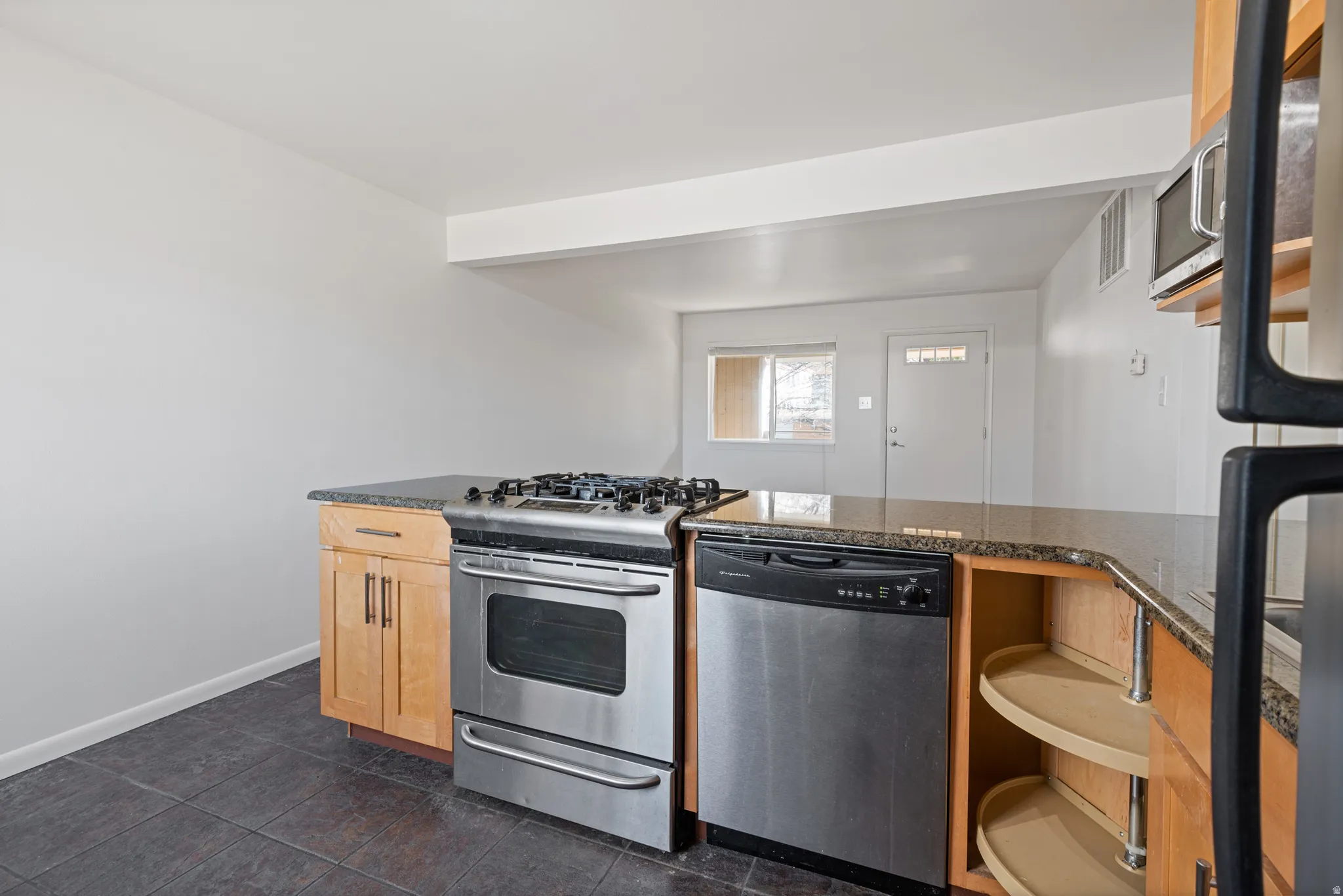 Kitchen featuring appliances with stainless steel finishes, dark stone countertops, light brown cabinetry, and dark tile patterned flooring
