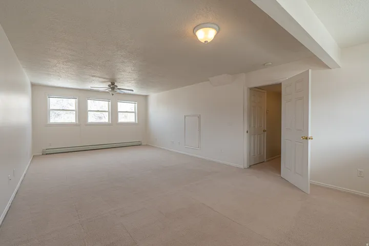 Unfurnished room with a textured ceiling, a baseboard heating unit, light carpet, and a ceiling fan