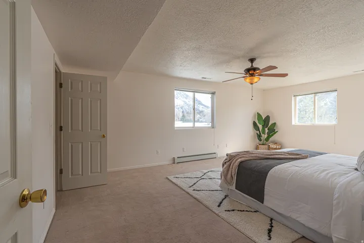 Carpeted bedroom featuring multiple windows, a baseboard radiator, a textured ceiling, and a ceiling fan