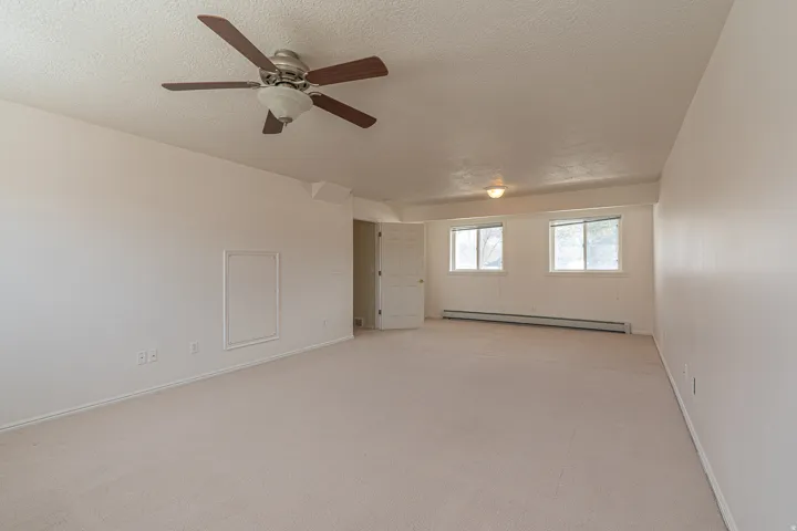 Empty room featuring light colored carpet, a baseboard radiator, a textured ceiling, and a ceiling fan