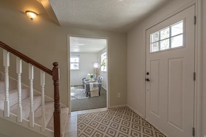 Foyer entrance featuring a textured ceiling, stairway, light colored carpet, and light tile patterned floors