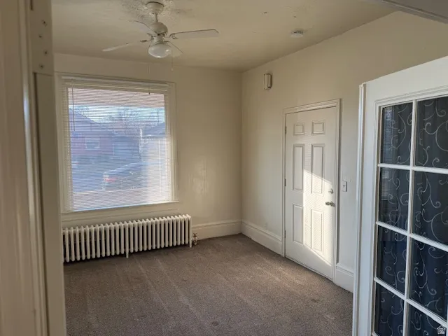 Empty room with radiator, carpet, and a ceiling fan