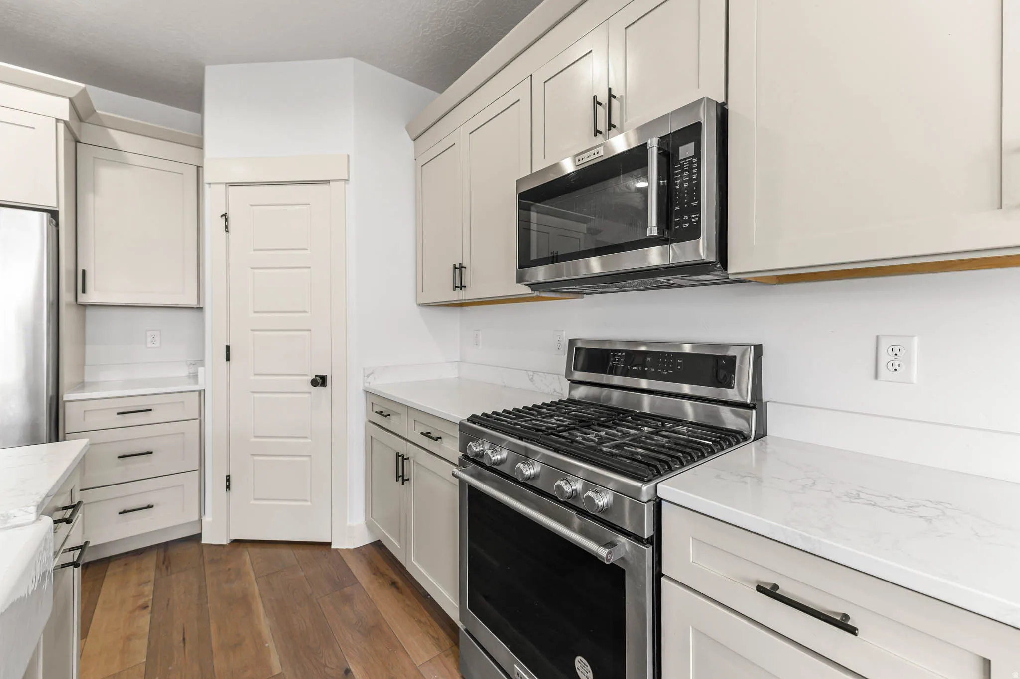Kitchen with stainless steel appliances, dark wood-style floors, and light stone counters