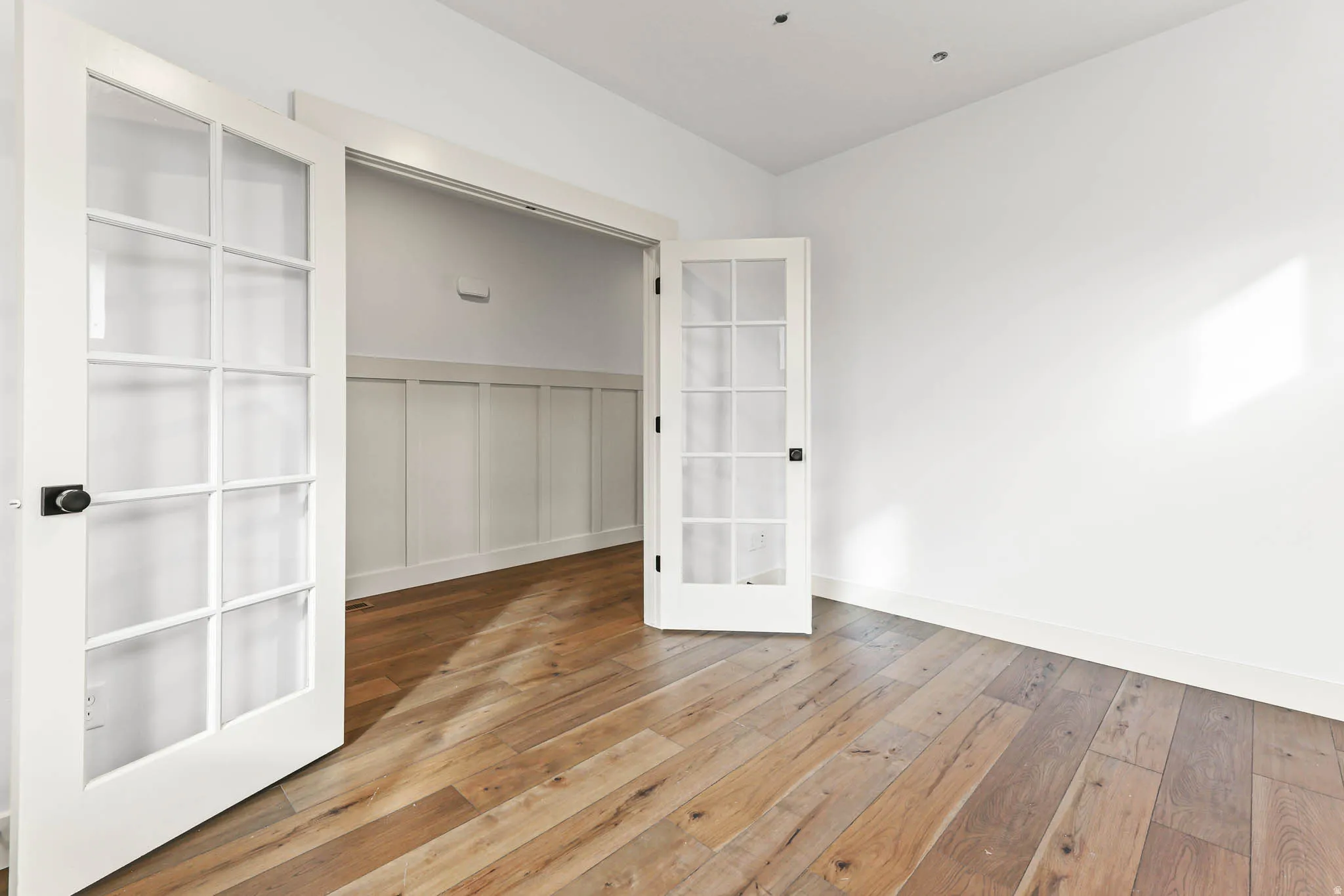 Unfurnished bedroom with light wood finished floors, a decorative wall, french doors, and wainscoting