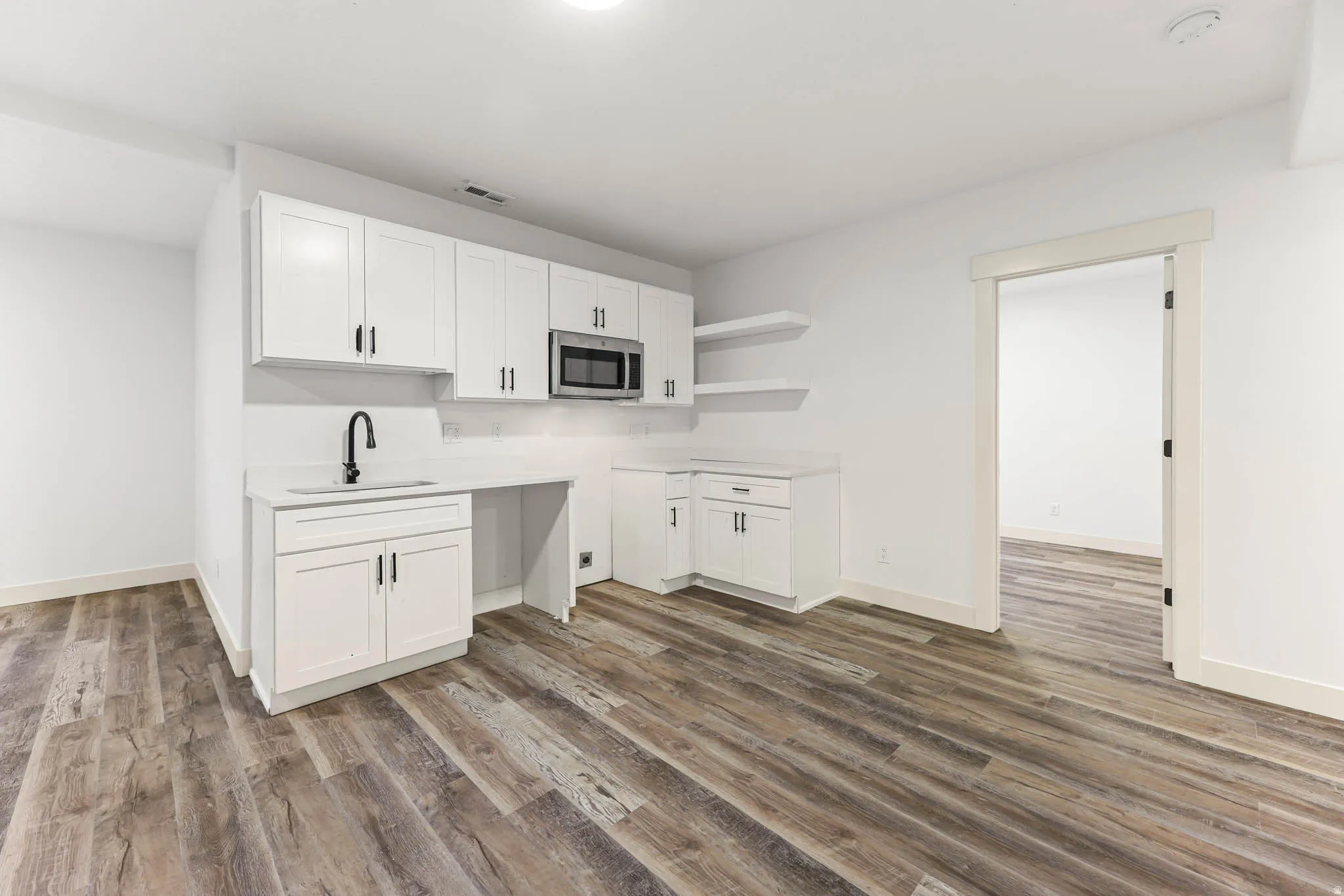 Kitchen with white cabinets, open shelves, stainless steel microwave, and dark wood-style floors