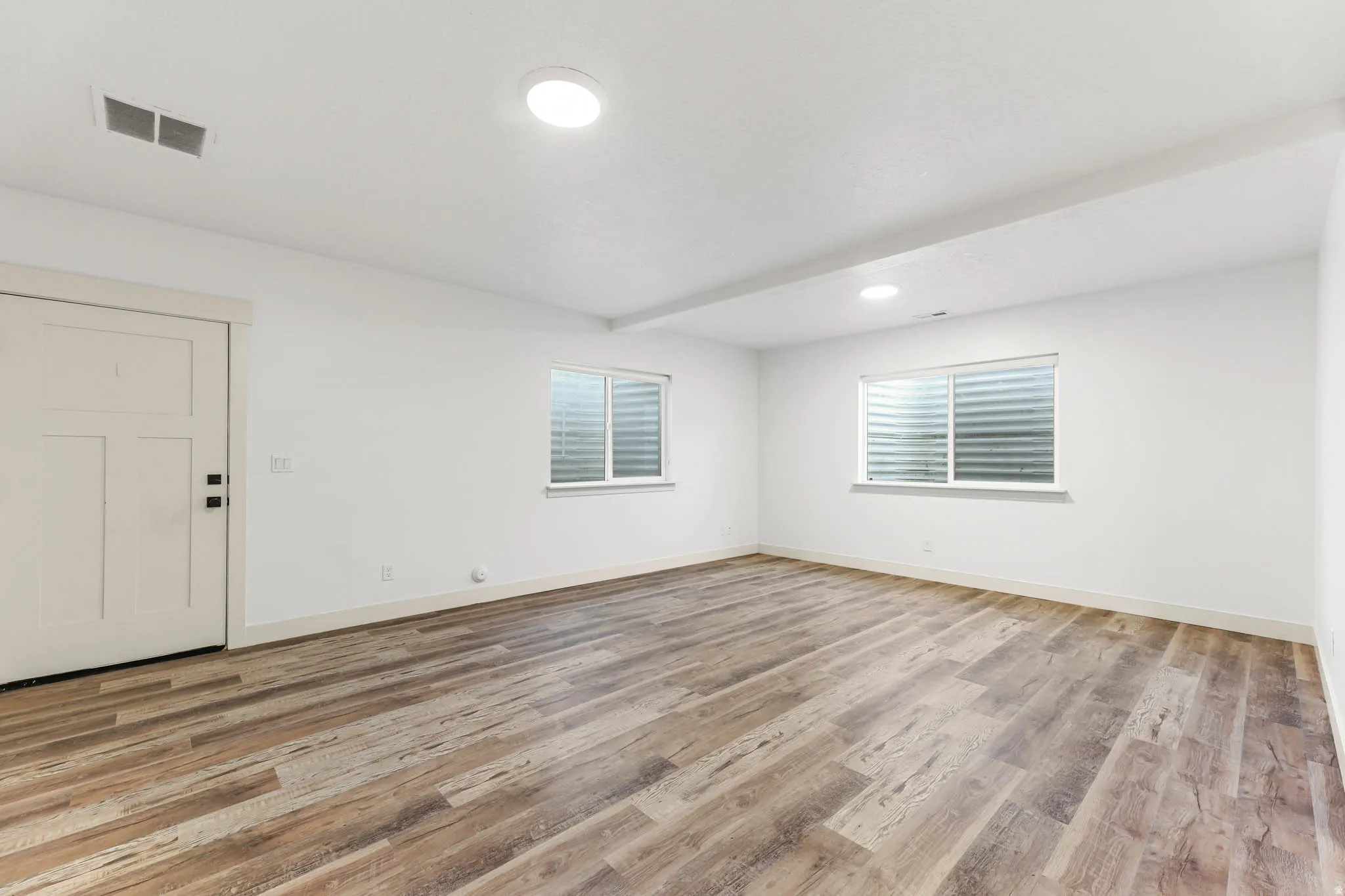 Empty room featuring light wood-style floors, beam ceiling, and recessed lighting